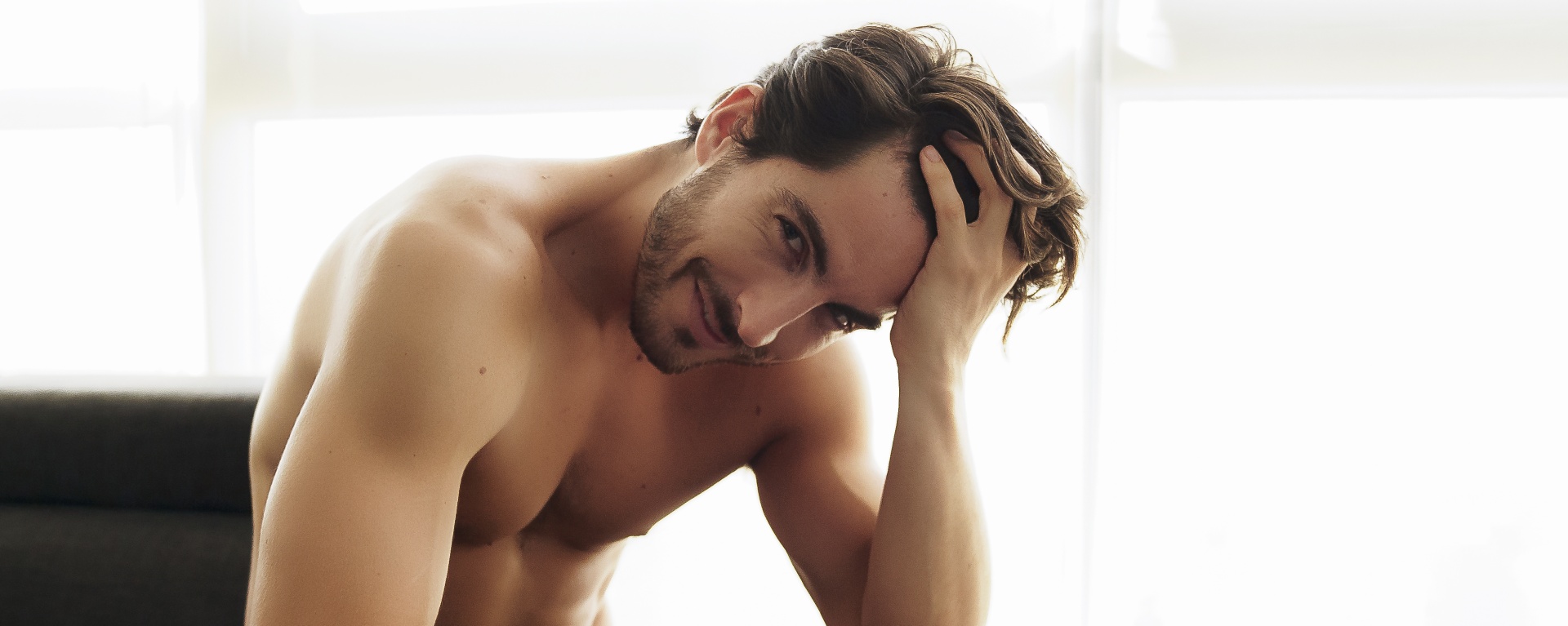 Portrait of Young Shirtless White Man With Beautiful Hair is smiling and looking at the camera. Athletic and Muscular Caucasian Male With fingers Through His Hair Looking Confident