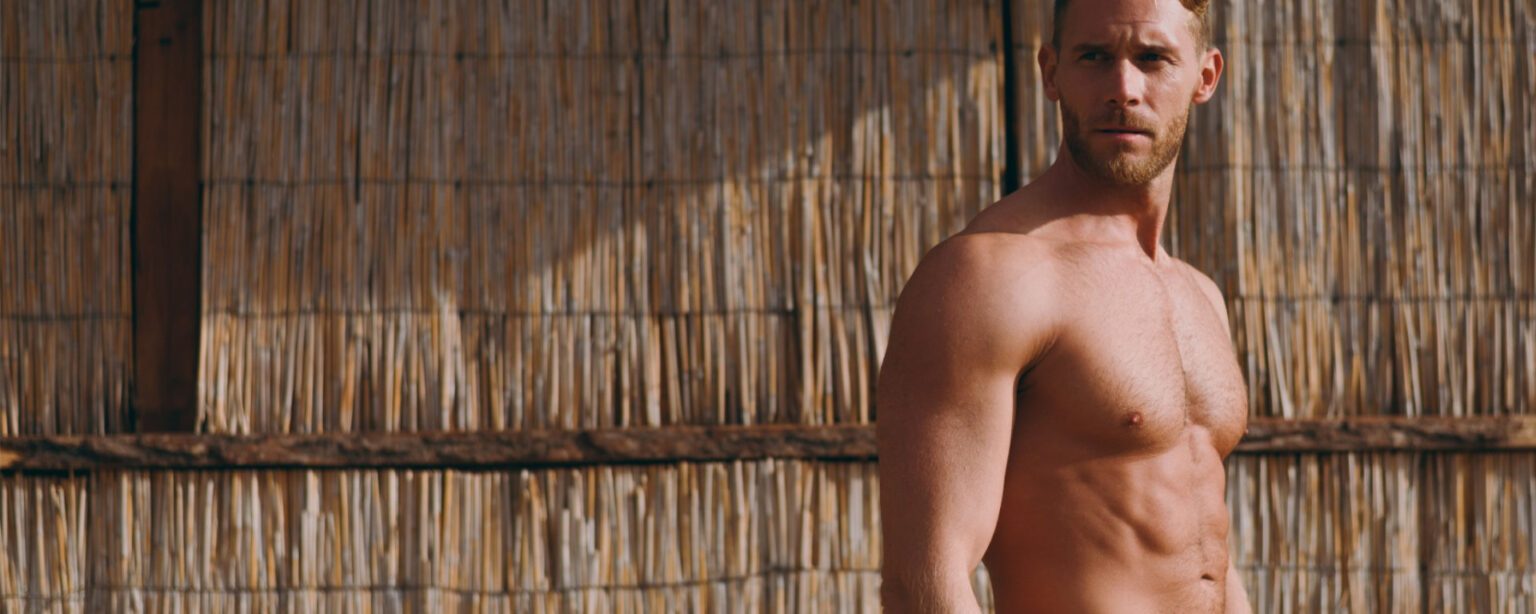 Side profile view young strong sporty athletic toned fit sportsman man wear shorts with naked torso look aside stand near straw wall after warm up training on sea beach outdoor in summer day morning