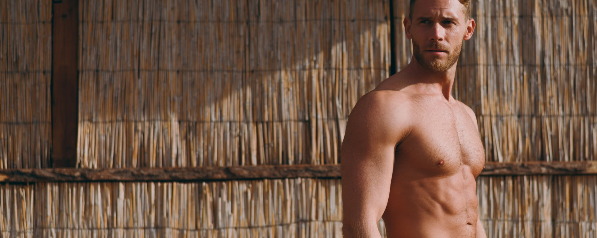 Side profile view young strong sporty athletic toned fit sportsman man wear shorts with naked torso look aside stand near straw wall after warm up training on sea beach outdoor in summer day morning