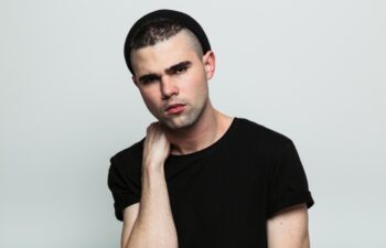 Studio portrait of serious man wearing black t-shirt looking at camera with hand on neck.
