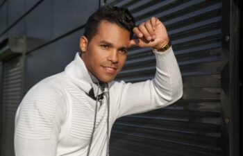 Portrait of a happy attractive Latino man with a smile on his face in stylish white casual clothes on a black background outside.